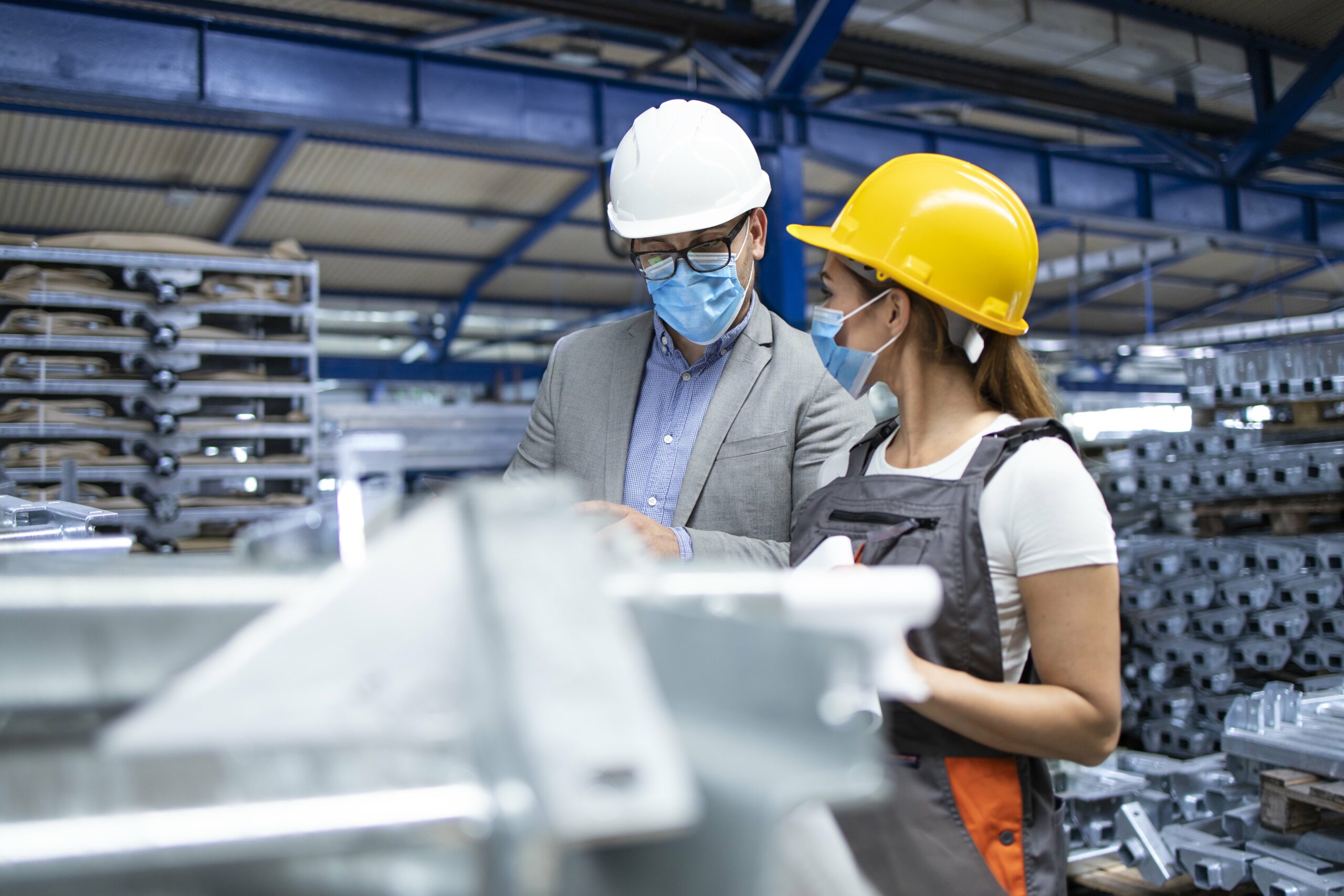 Industrial supervisor manager with hygienic mask talking with worker in production factory.